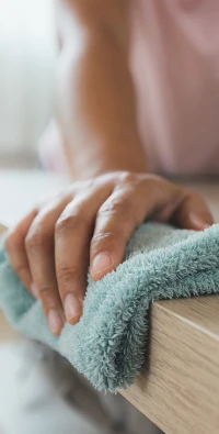 水色の布を使って木の表面を掃除している人のクローズアップ。.