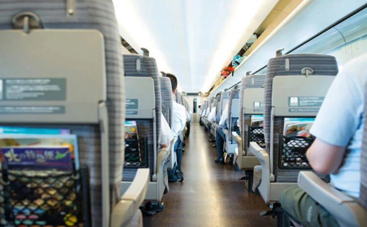 座席の列、頭上の荷物置き場、雑誌が入った座席の背もたれのポケットを備えた旅客列車の内部の様子。.