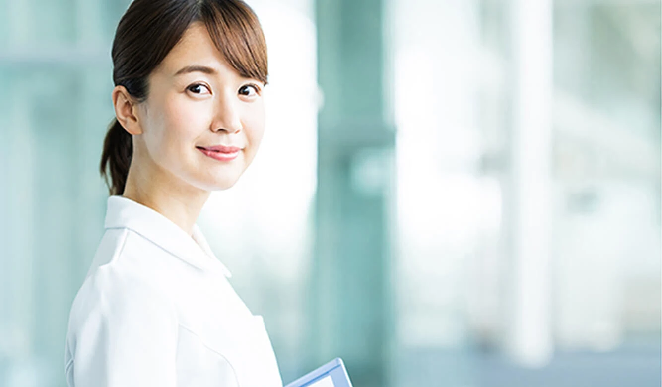 白衣を着た女性が、明るくぼやけた背景の中で、フォルダーを持って微笑んでいます。.