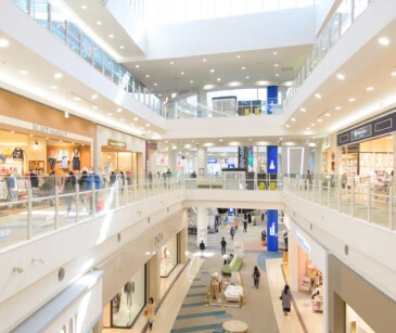 さまざまな店舗、明るい照明、上階と下階の両方の店舗の前を歩く人々がある多層ショッピングモール。.