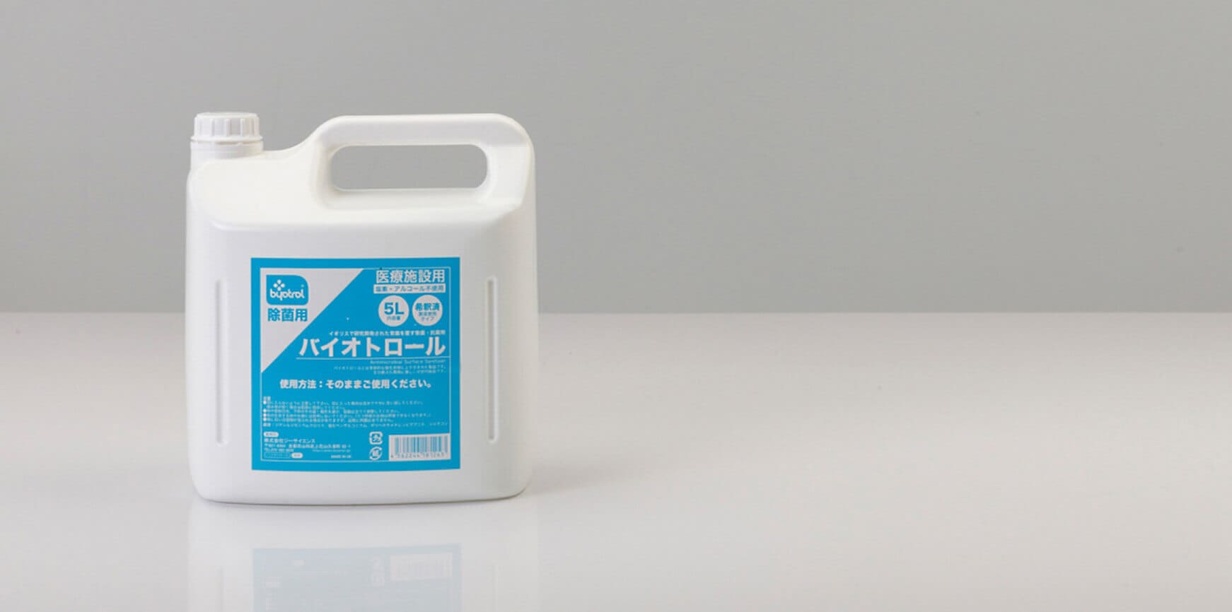 反射面に配置された、青いラベルとハンドルが付いた白いプラスチック容器。製品情報を示す可能性のあるテキストとグラフィックが含まれています。.