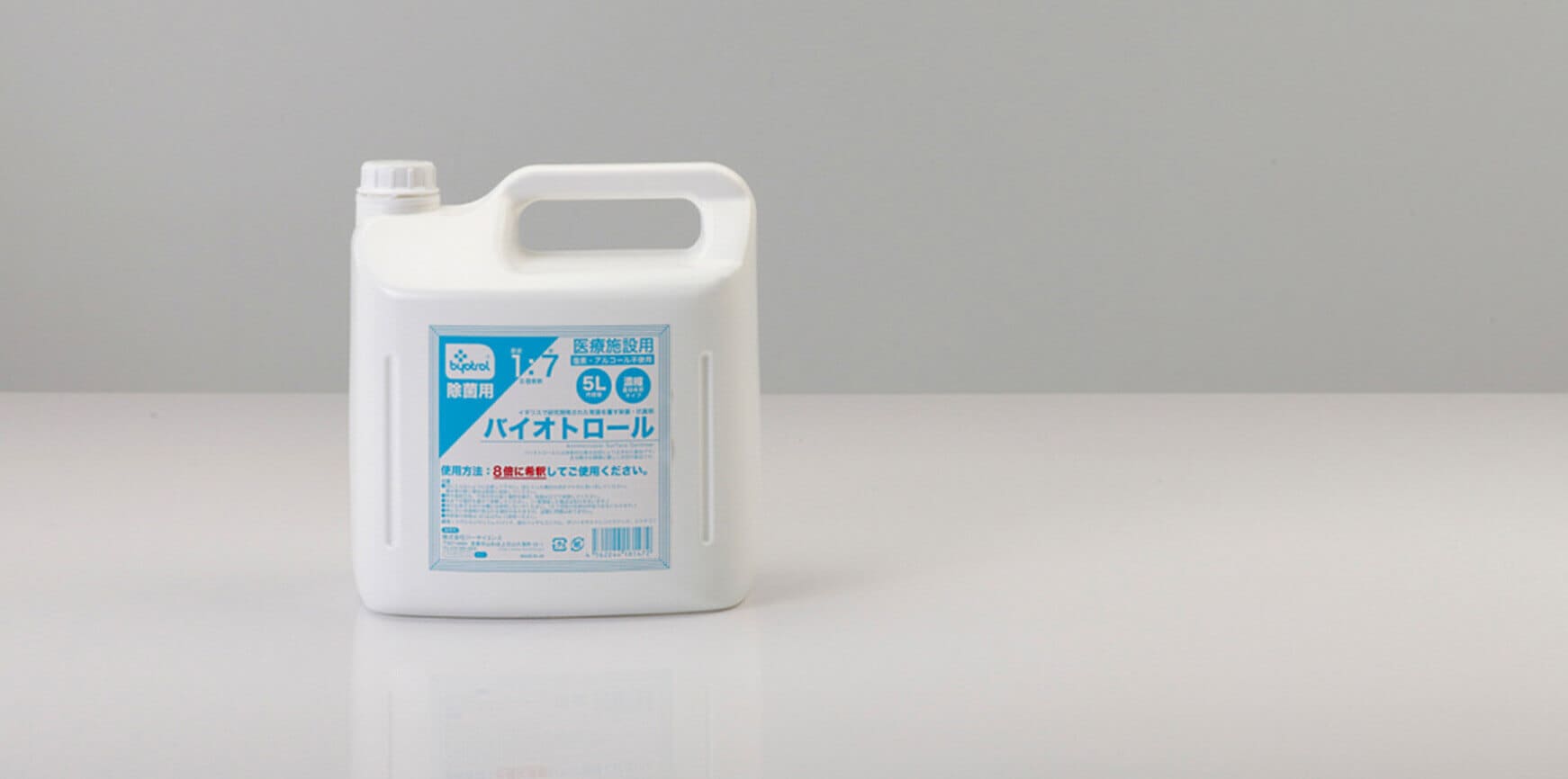 青と白のラベルが付いた白いプラスチックの水差しが、平らな面に置かれています。ラベルには日本語の文字と記号が記載されています。水差しには一体型のハンドルと上部にねじ式のキャップが付いています。.