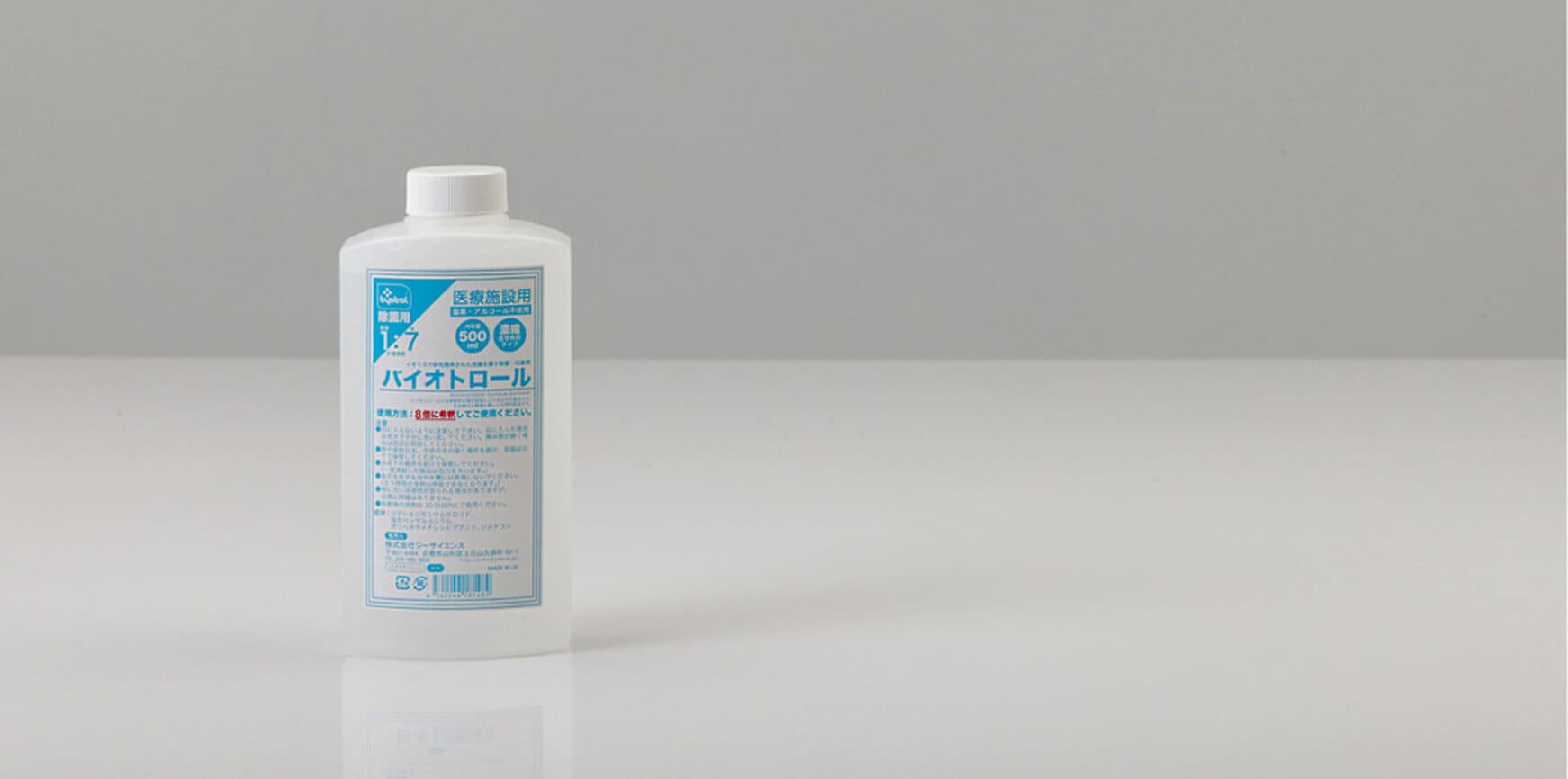 青と白のラベルが付いた白いボトルが、無地の灰色の背景の反射面の上に置かれています。.