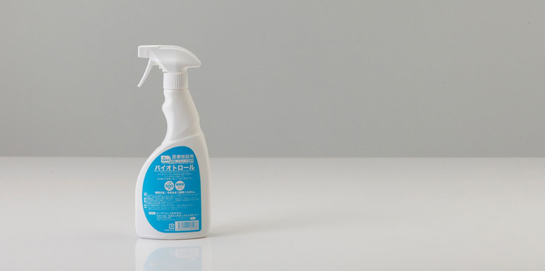 灰色の背景に、反射する白い表面の上に青いラベルが付いた白いスプレーボトルが立っています。.