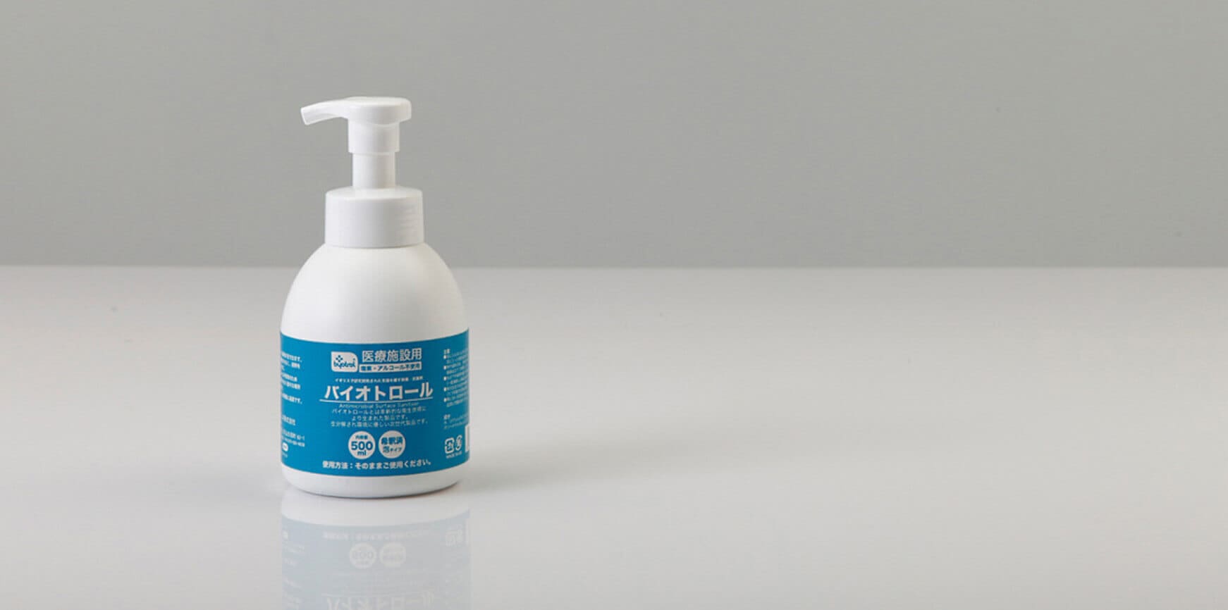 無地のライトグレーの表面に青いラベルが付いた白いポンプボトル。.