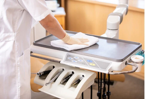 白衣を着た人が白い布で歯科用トレーを拭いています。トレーには歯科用器具や機器が入っています。.