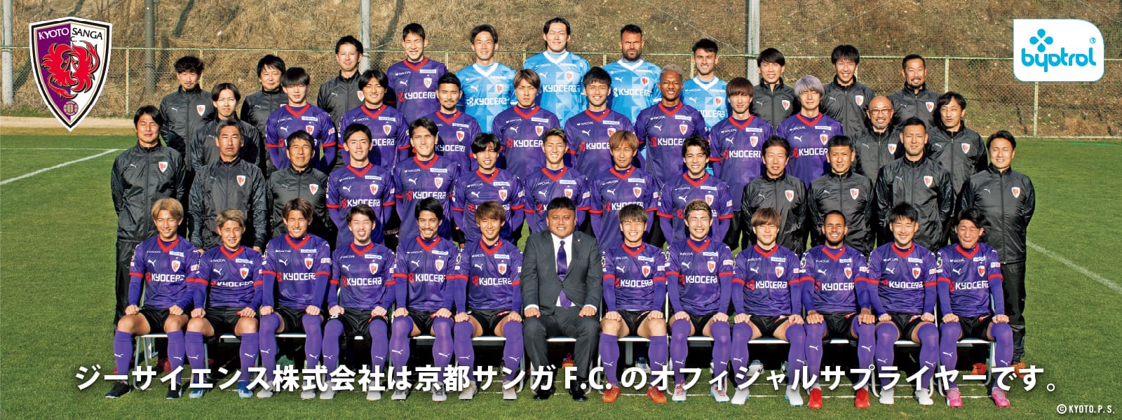 紫と黒のユニフォームを着た選手とスタッフが屋外の芝生の上でポーズをとるスポーツチームの集合写真。チームのロゴは、ブプロピオンのロゴとオフィシャルサプライヤーのマークと並んで左上に表示されます。本文は日本語で、京都サンガF.C.への加入を祝う内容となっている。 J1リーグで。.